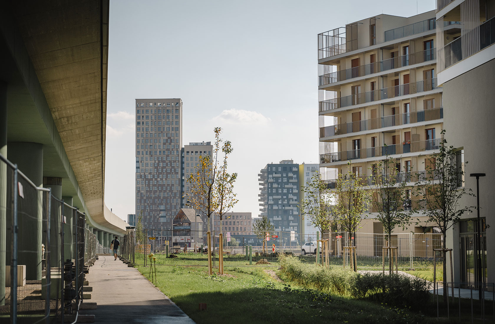 Modern urban area with tall apartment buildings, green spaces, and a pedestrian walkway under a bridge.