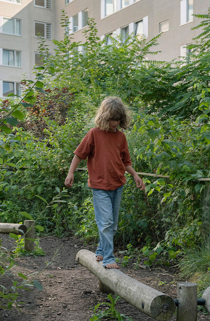 A child balancing on a raised log surrounded by greenery.