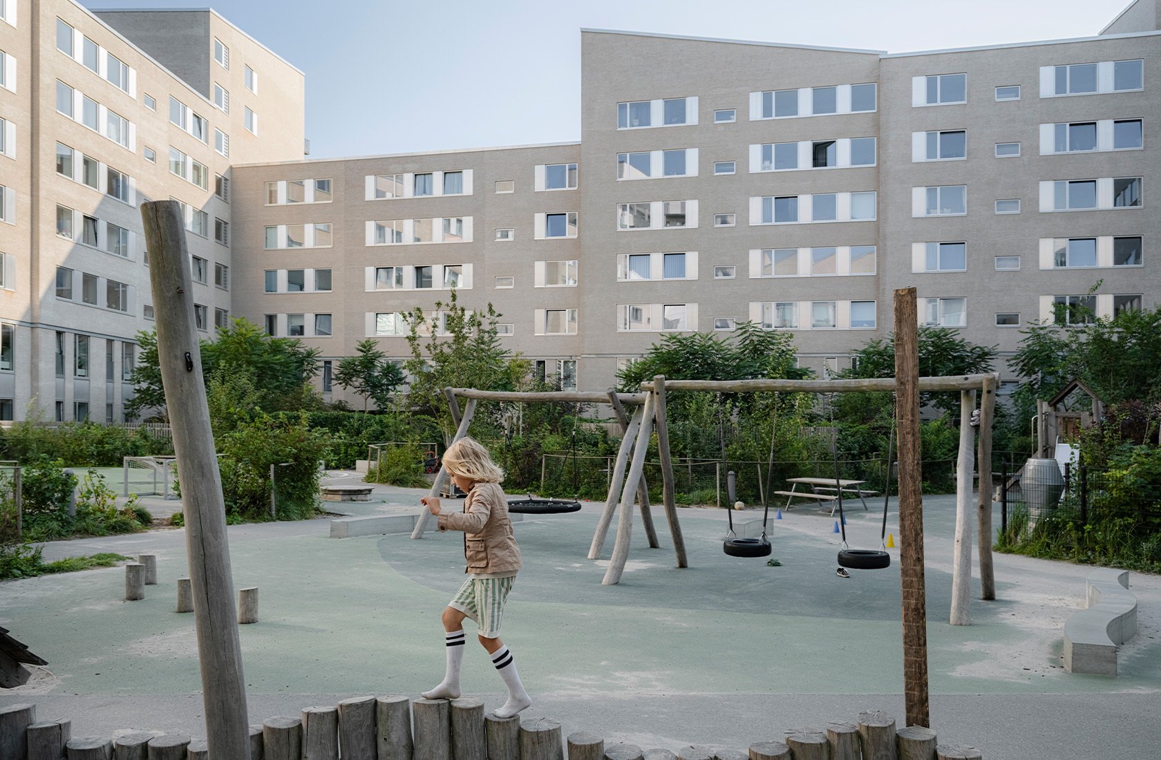 A child balancing on a larger playground surrounded by gray high-rise buildings.
