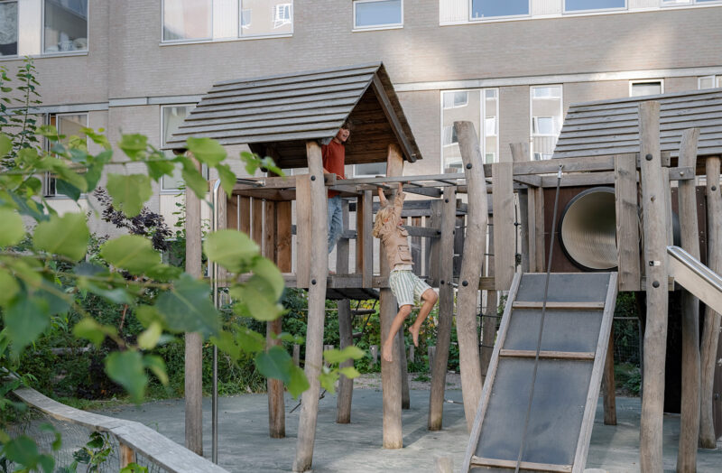Two children playing and hanging on a climbing frame in a yard surrounded by gray high-rise buildings.