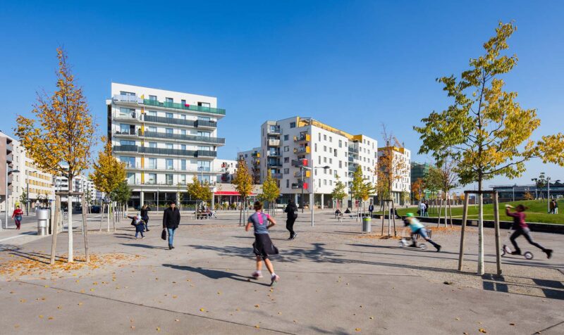 People moving around a square in front of high-rise buildings.