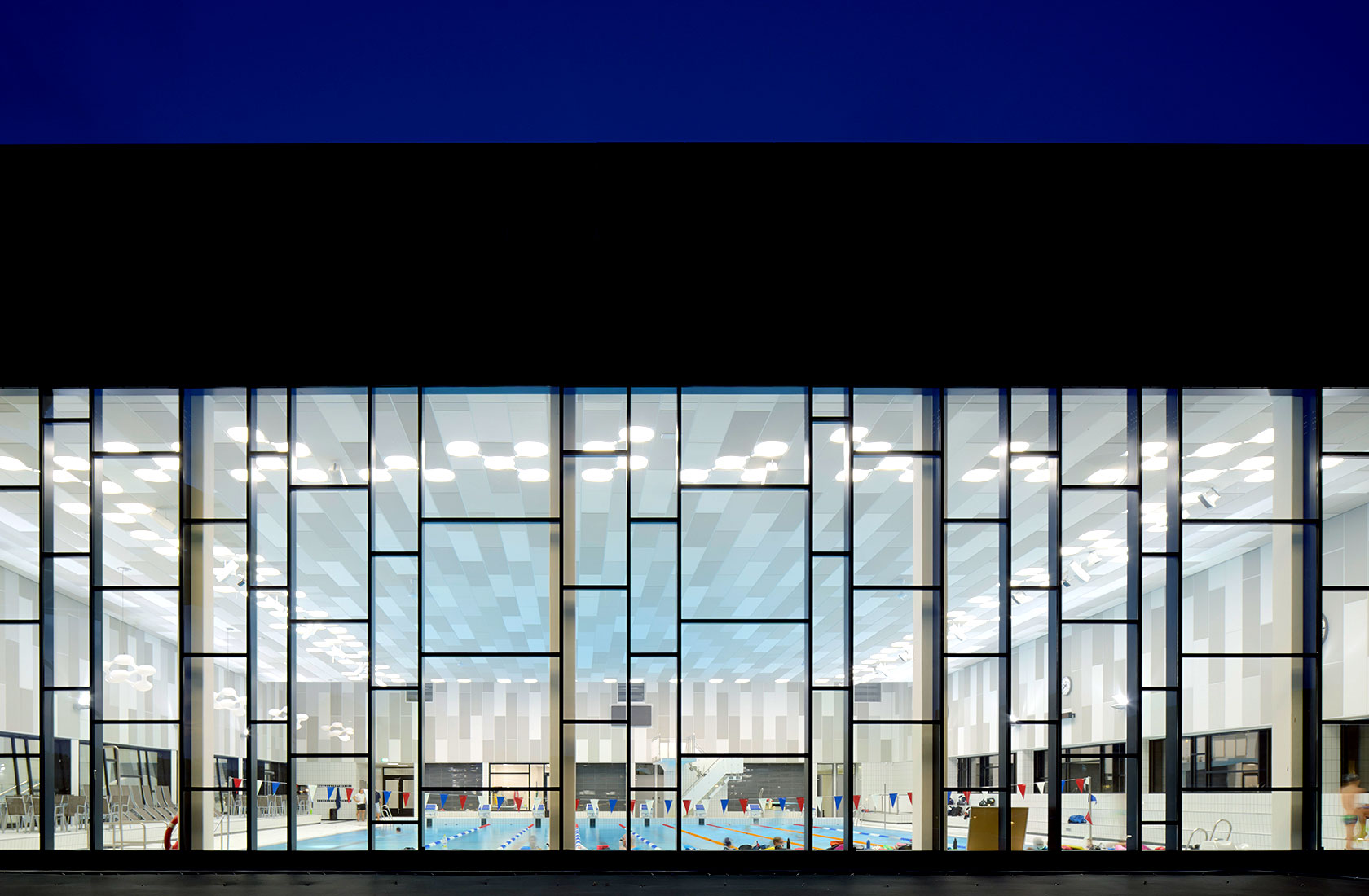 Swimming hall with a large pool seen from the outside through a large window area.