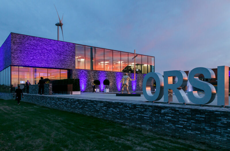 Modern building with large ORSI sign, glass windows at dusk with purple lighting.