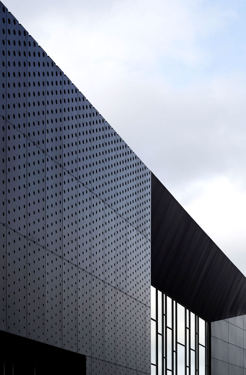 Facade section in black metal with a perforated pattern and a large window section with glass in various sizes.