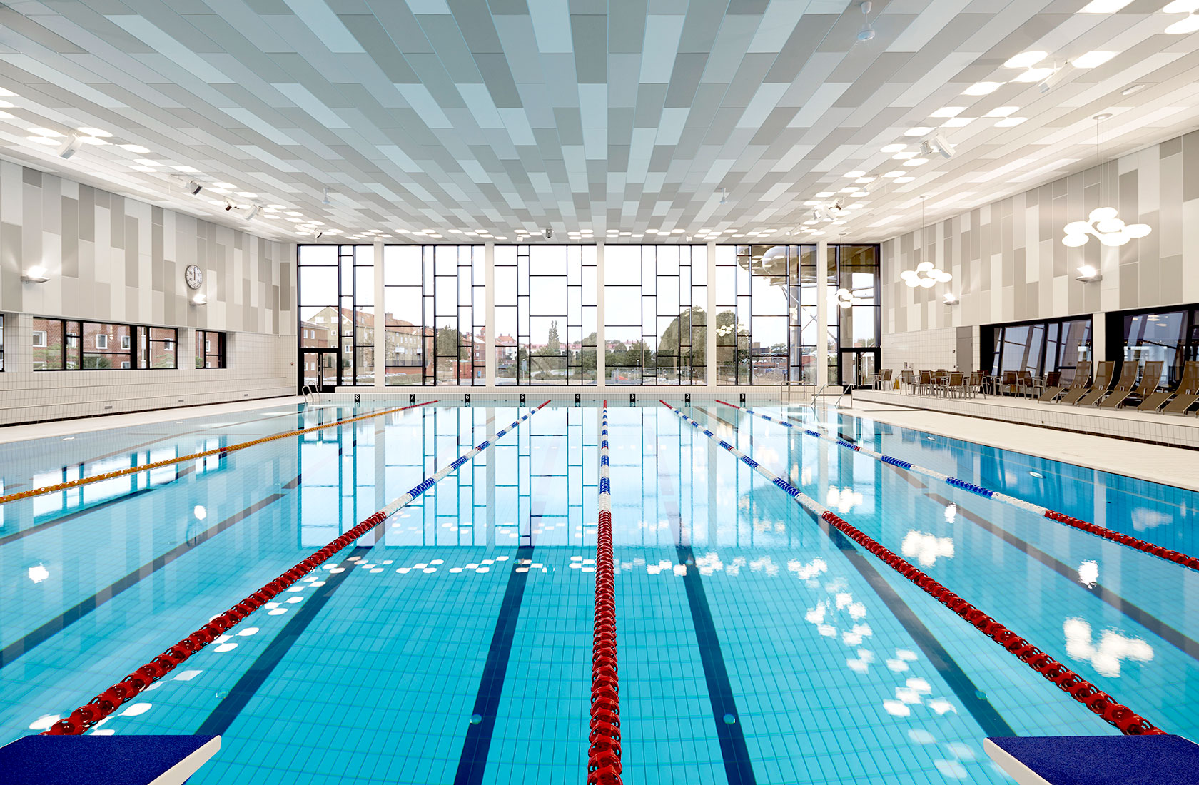 Empty swimming pool with lanes for competition, exercise swimming, and a large window section in the background.