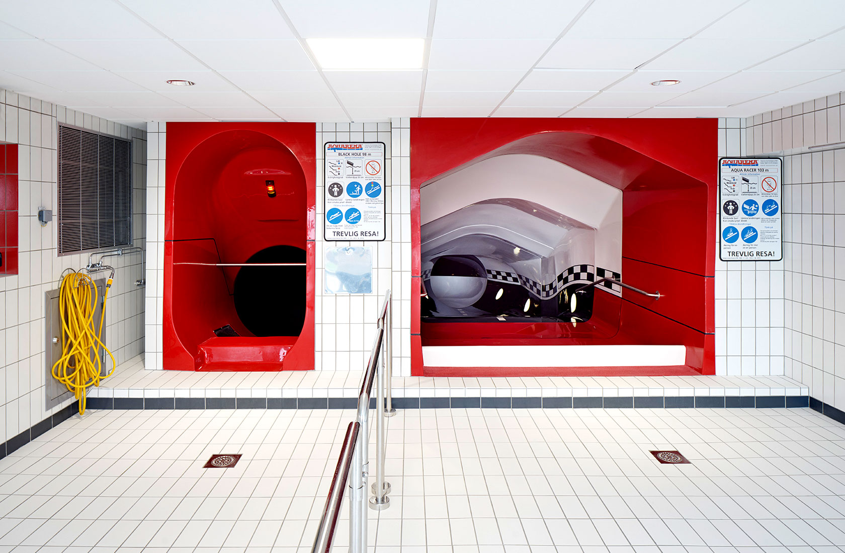 Entrance area to two different water slides in red plastic with floors and walls in white tiles.