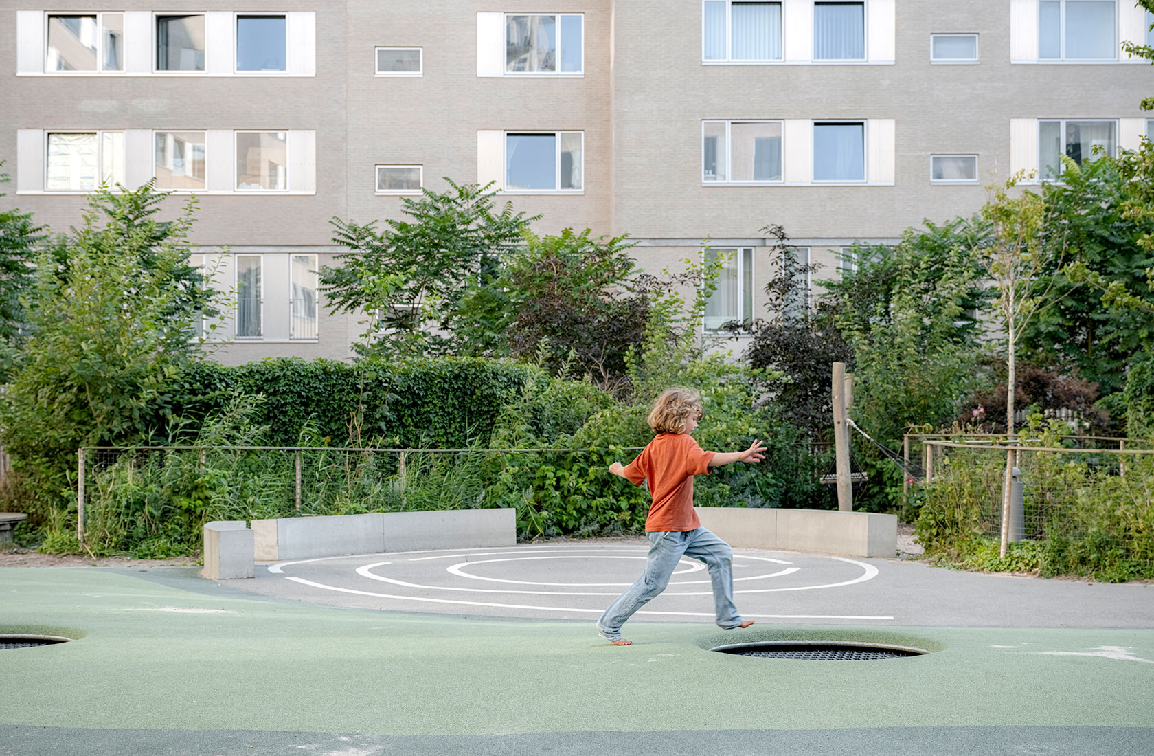 A child in a playground with a gray high-rise buildings in the background.
