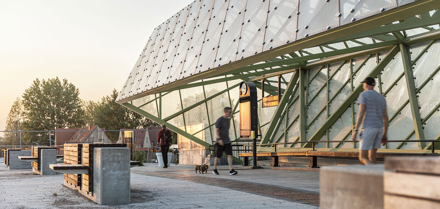 Modern train station platform with people walking and benches, during sunset.