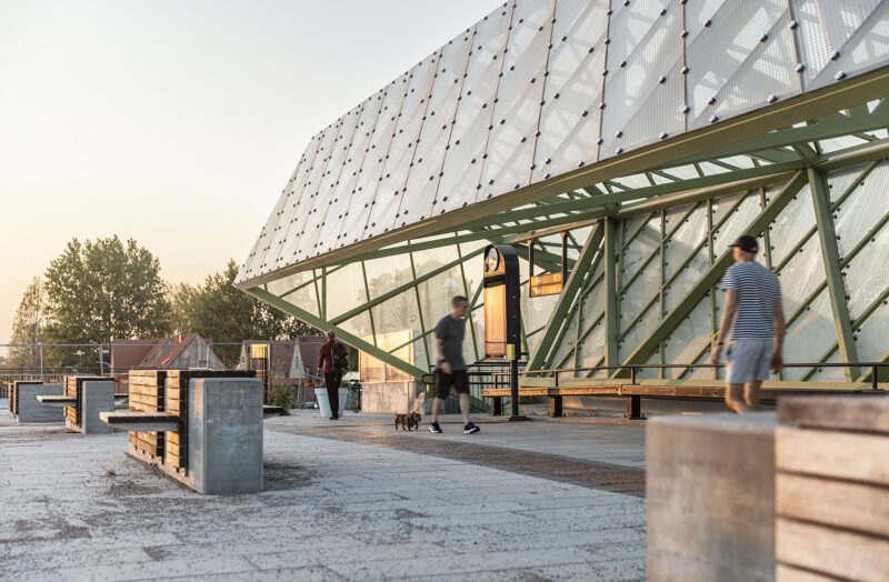 Modern train station platform with people walking and benches, during sunset.
