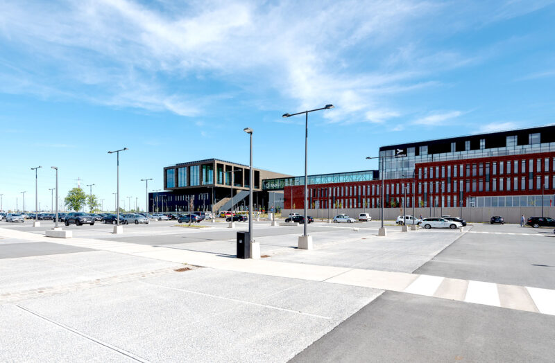 Modern hospital building with large parking lot under a clear blue sky.