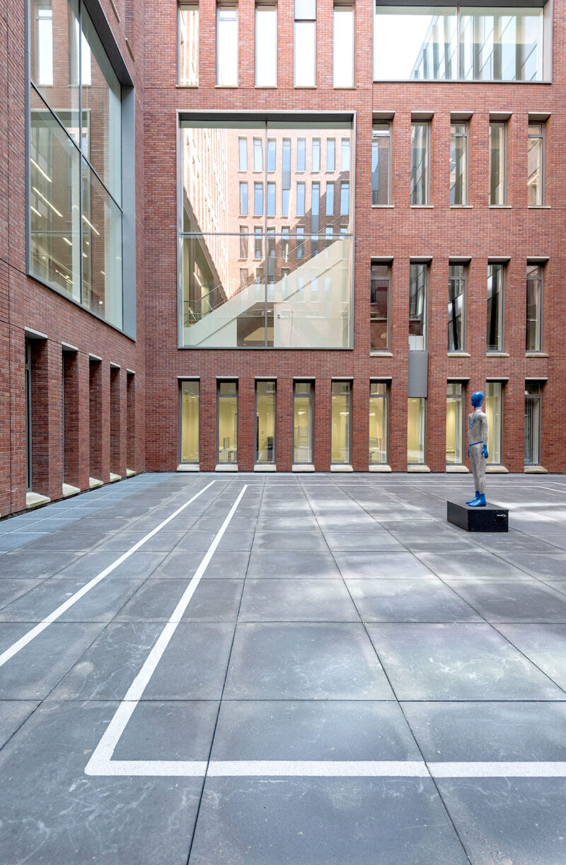 Modern courtyard with red brick architecture and a blue statue on a pedestal in the foreground.