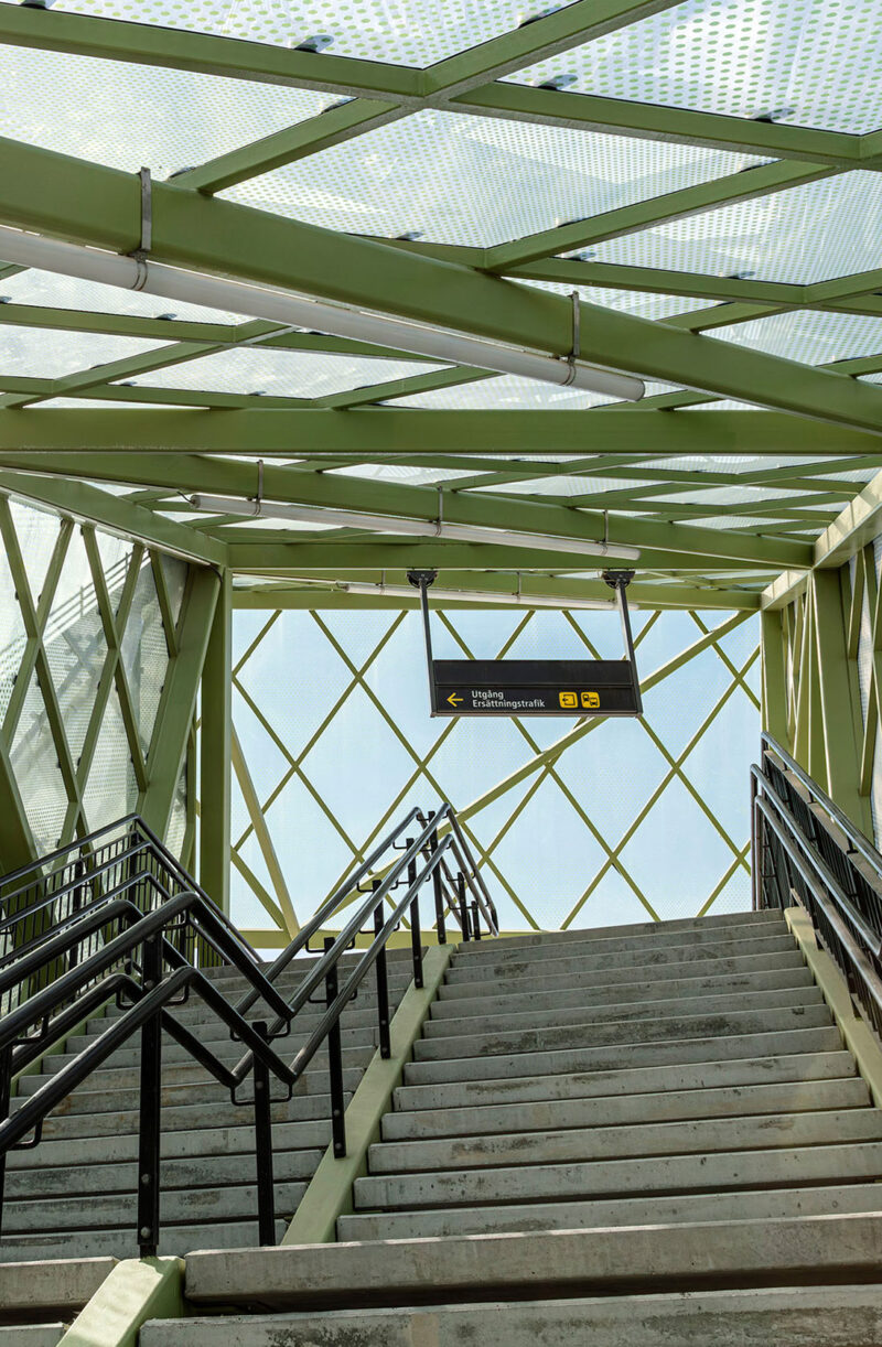 Concrete stairs from train platform leading up to a green lattice structure with a sign for replacement traffic.