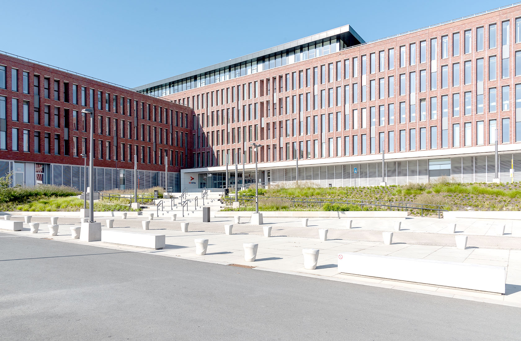 Modern brick hospital building with many windows and a landscaped exterior on a sunny day.