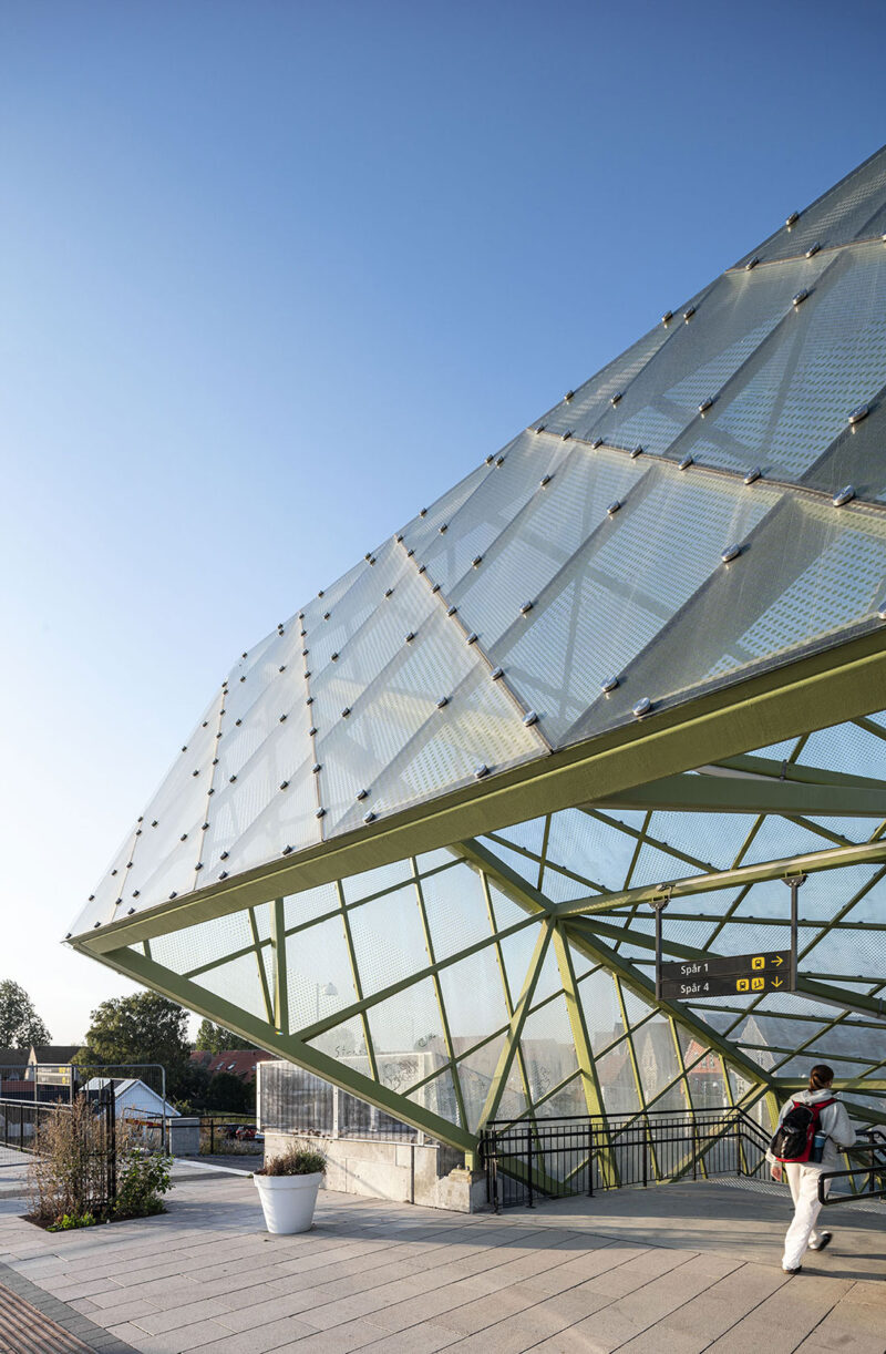 Modern glass and steel architectural structure at a train station under a clear blue sky.