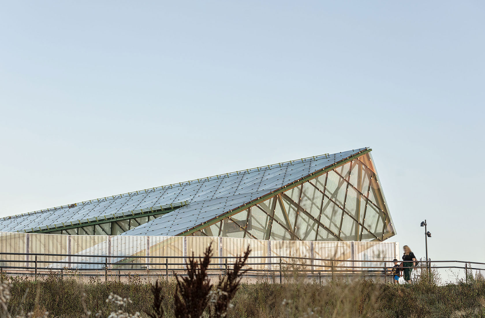 Train station with modern glass and metal building structure with pedestrians walking outside in daylight.