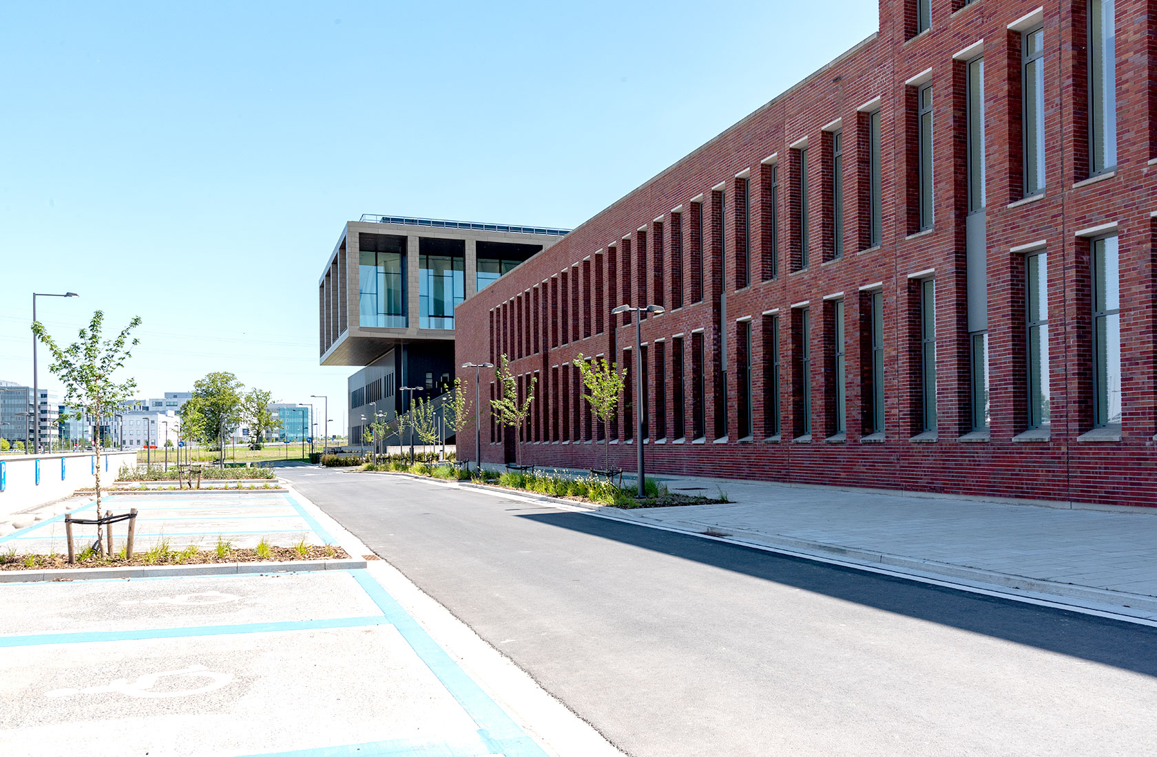 Modern brick hospital building with large windows and landscaped campus on a sunny day.