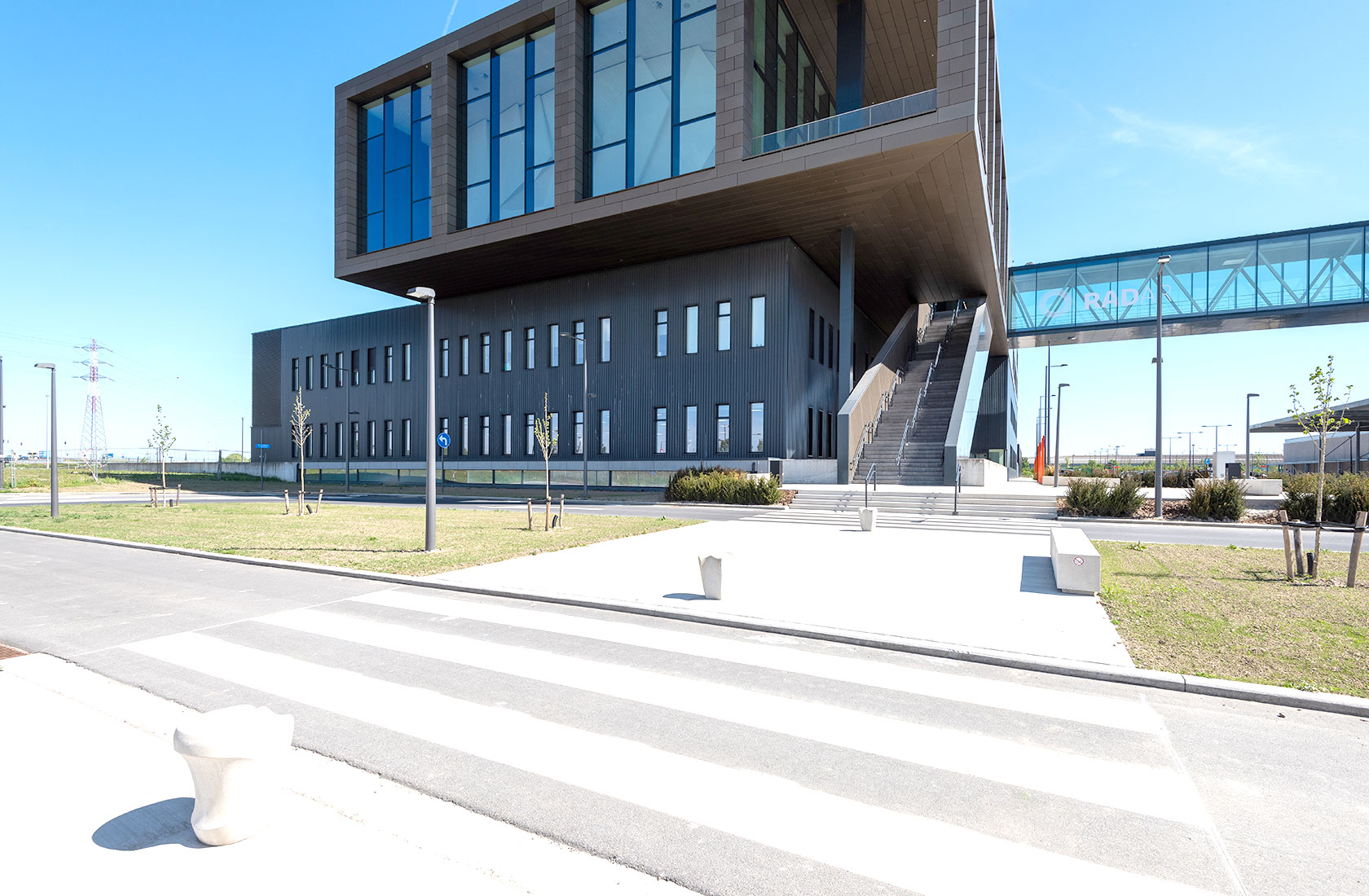 Modern hospital building with glass walkway, large windows, and outdoor stairs.