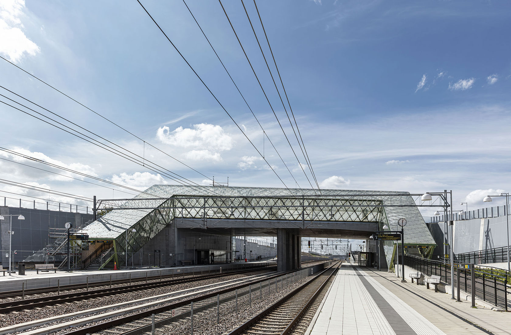 Modern train station with an overhead footbridge, clear sky and railway tracks extending forward.