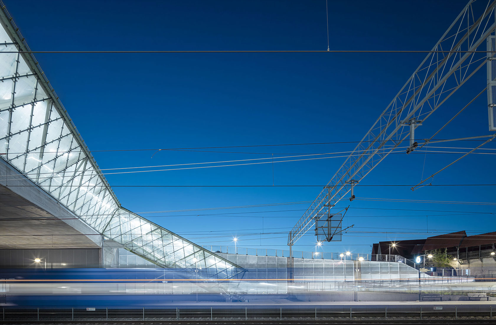Modern train station at night with a glass structure and illuminated platform.