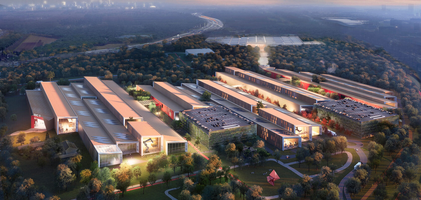 Aerial view of a modern industrial complex surrounded by trees with city skyline in the distance.