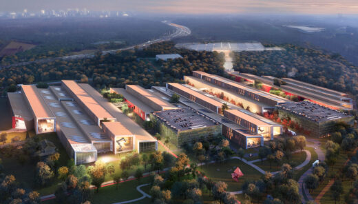 Aerial view of a modern industrial complex surrounded by trees with city skyline in the distance.