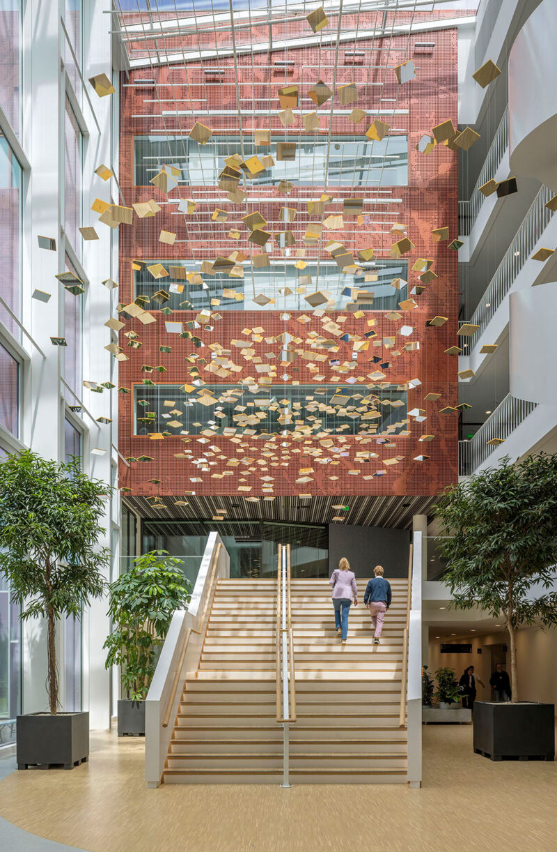 Modern atrium with staircase, hanging art installation, large windows, and indoor plants.