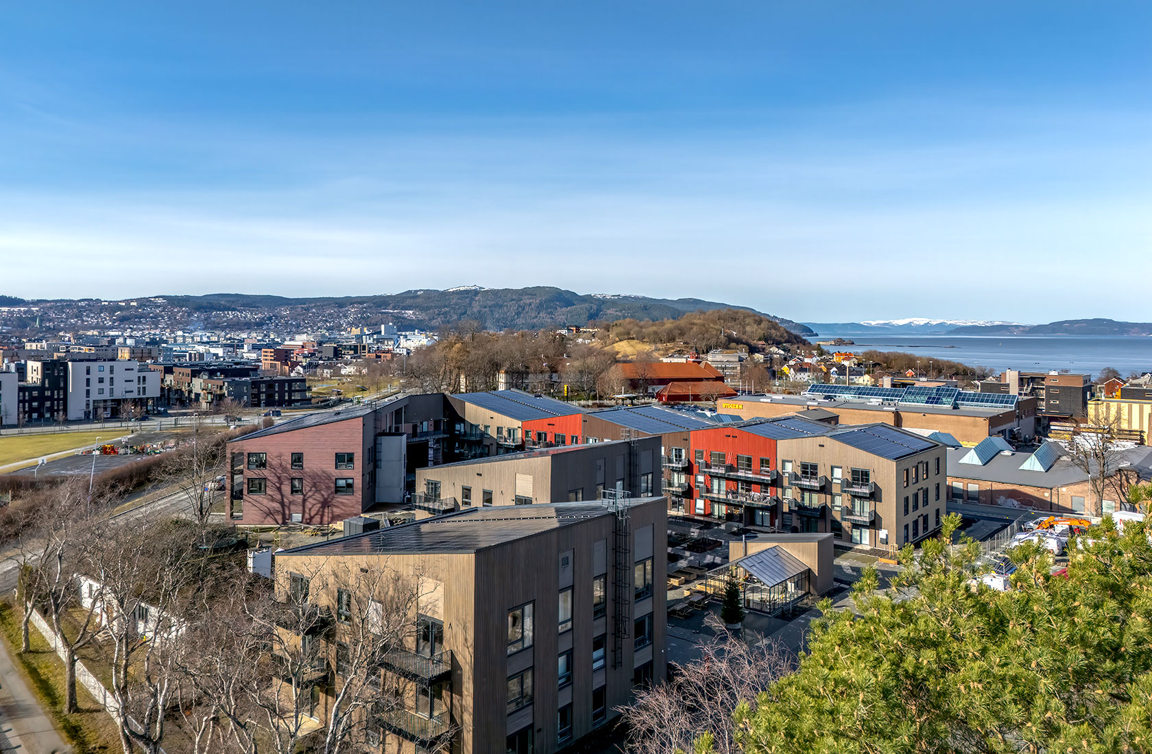 Aerial view of coastal city with modern buildings, blue sky, and distant snowy mountains.