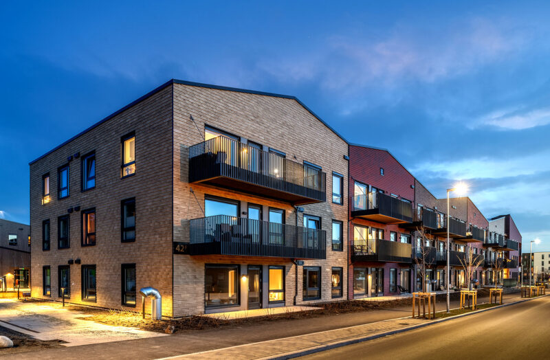 Modern apartment building with lit balconies at dusk seen from the street.