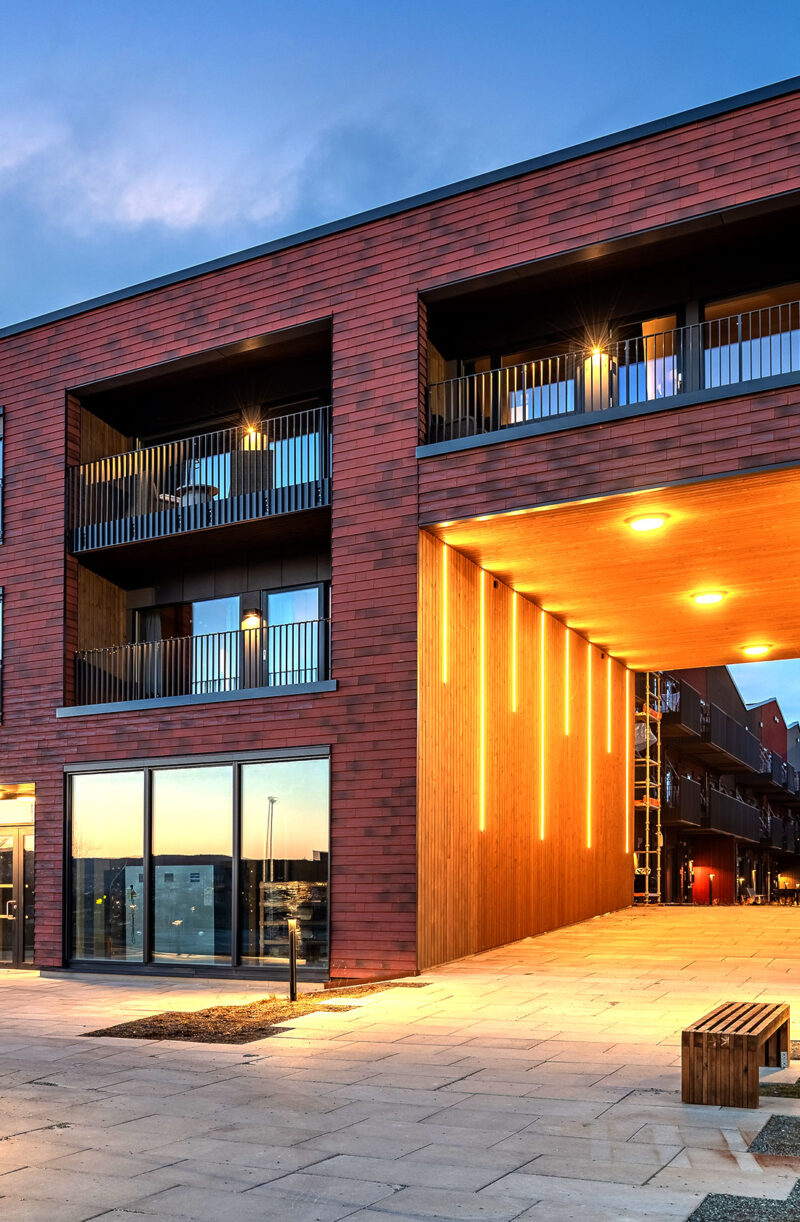 Modern apartment building at dusk with warm lighting and outdoor seating areas.