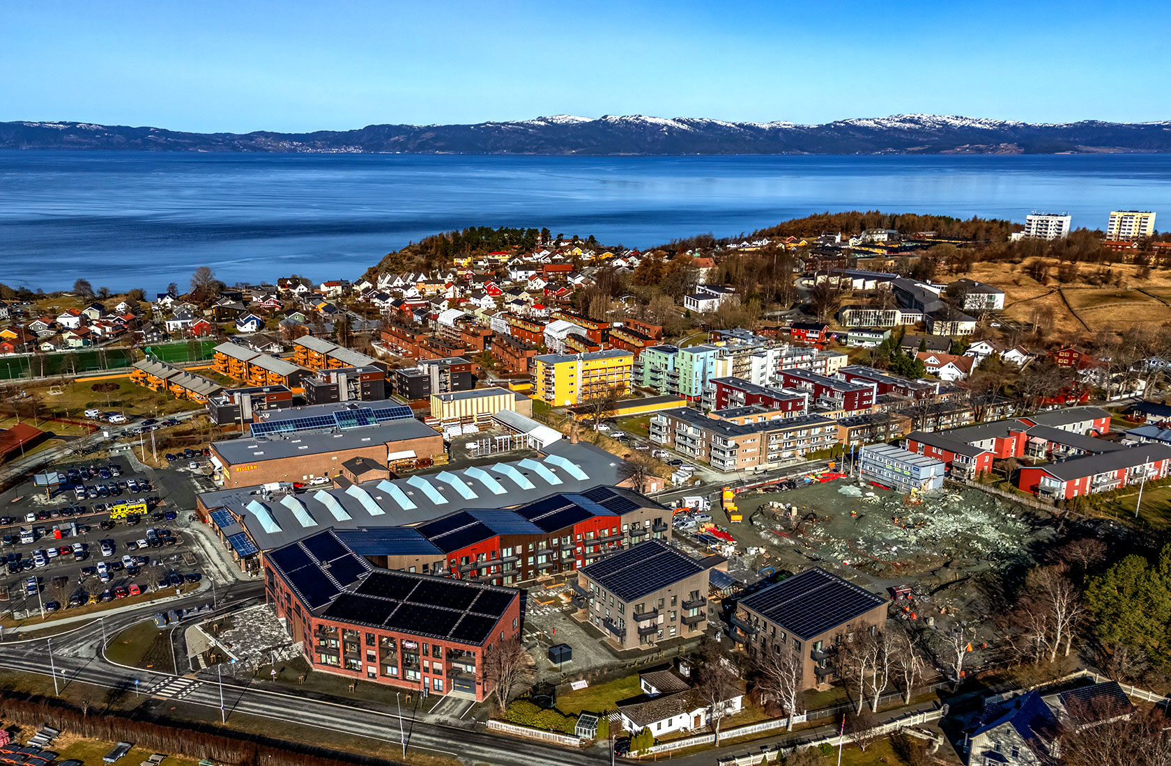 Aerial view of a coastal town with colorful buildings, construction sites, and mountains in the background.