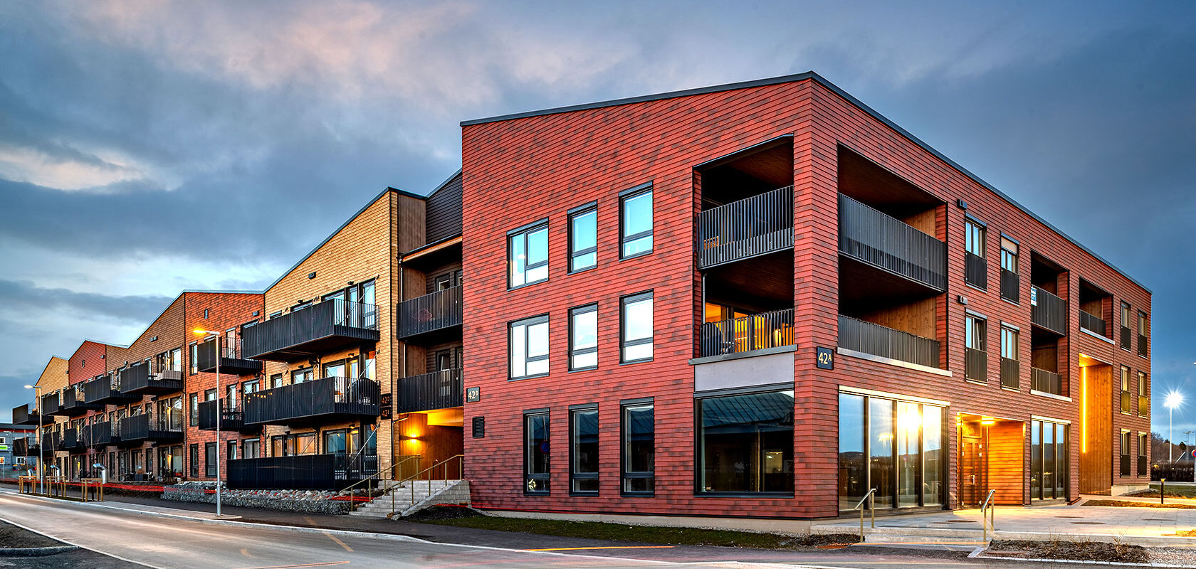 Modern red brick apartment building with balconies at dusk. Blue sky and street view.