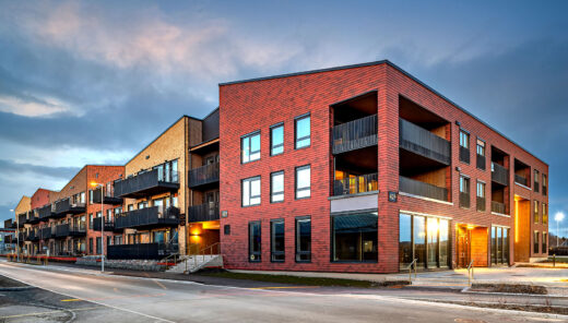 Modern red brick apartment building with balconies at dusk. Blue sky and street view.