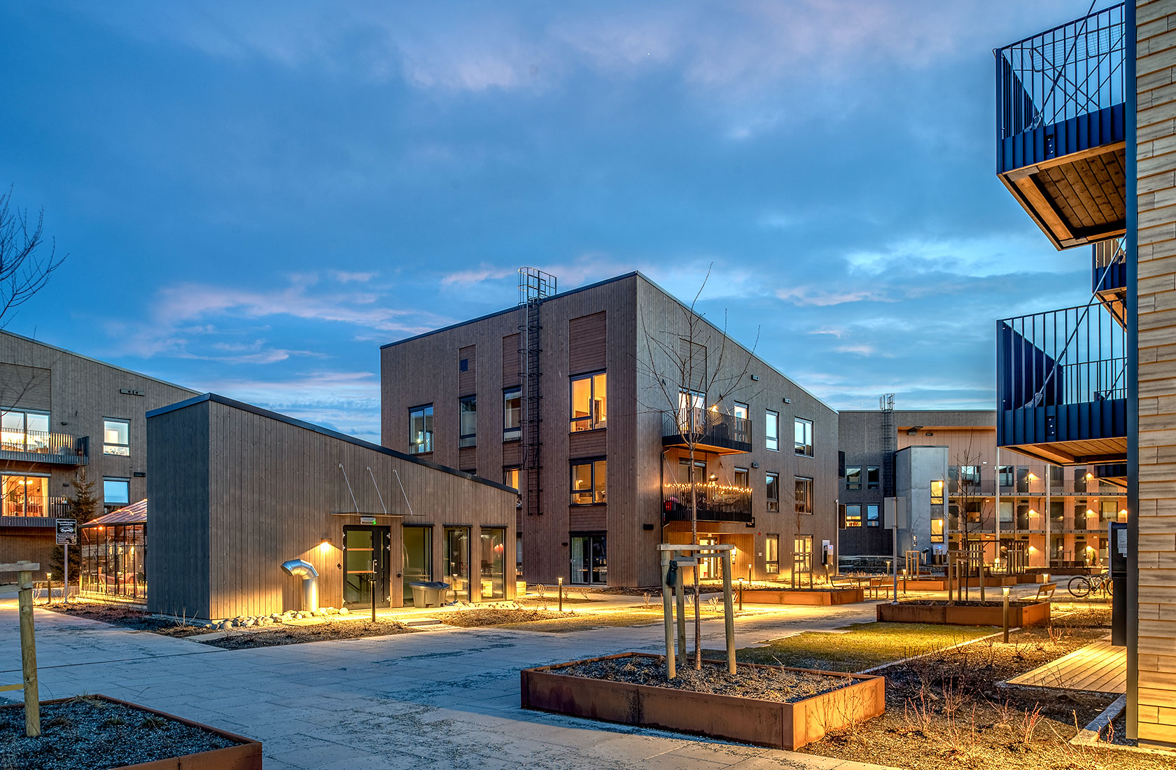 Modern apartment complex at dusk with illuminated windows and balconies and a blue sky backdrop.