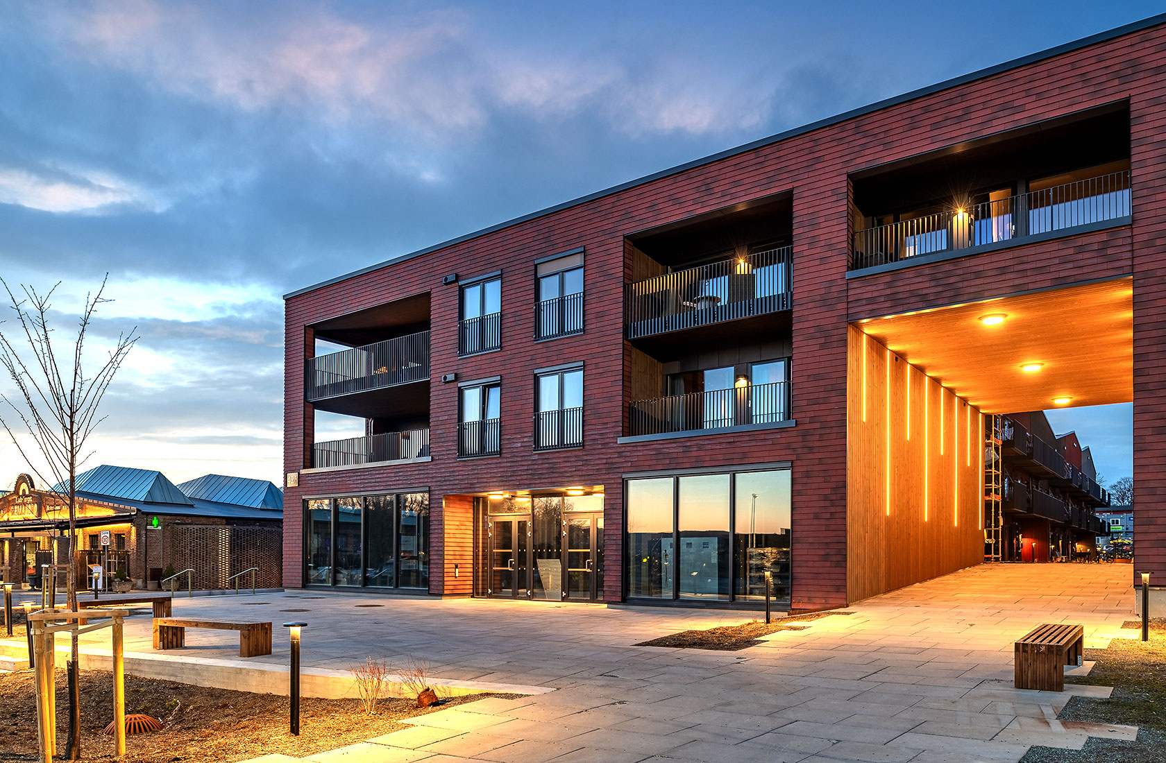 Modern brick apartment building with illuminated passageway at dusk.