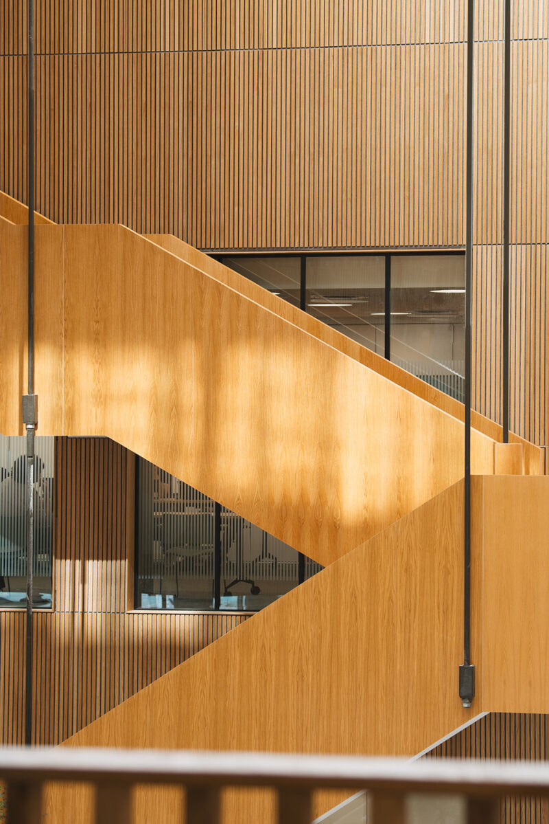 Modern wooden staircase with vertical slat paneling in a bright interior space.