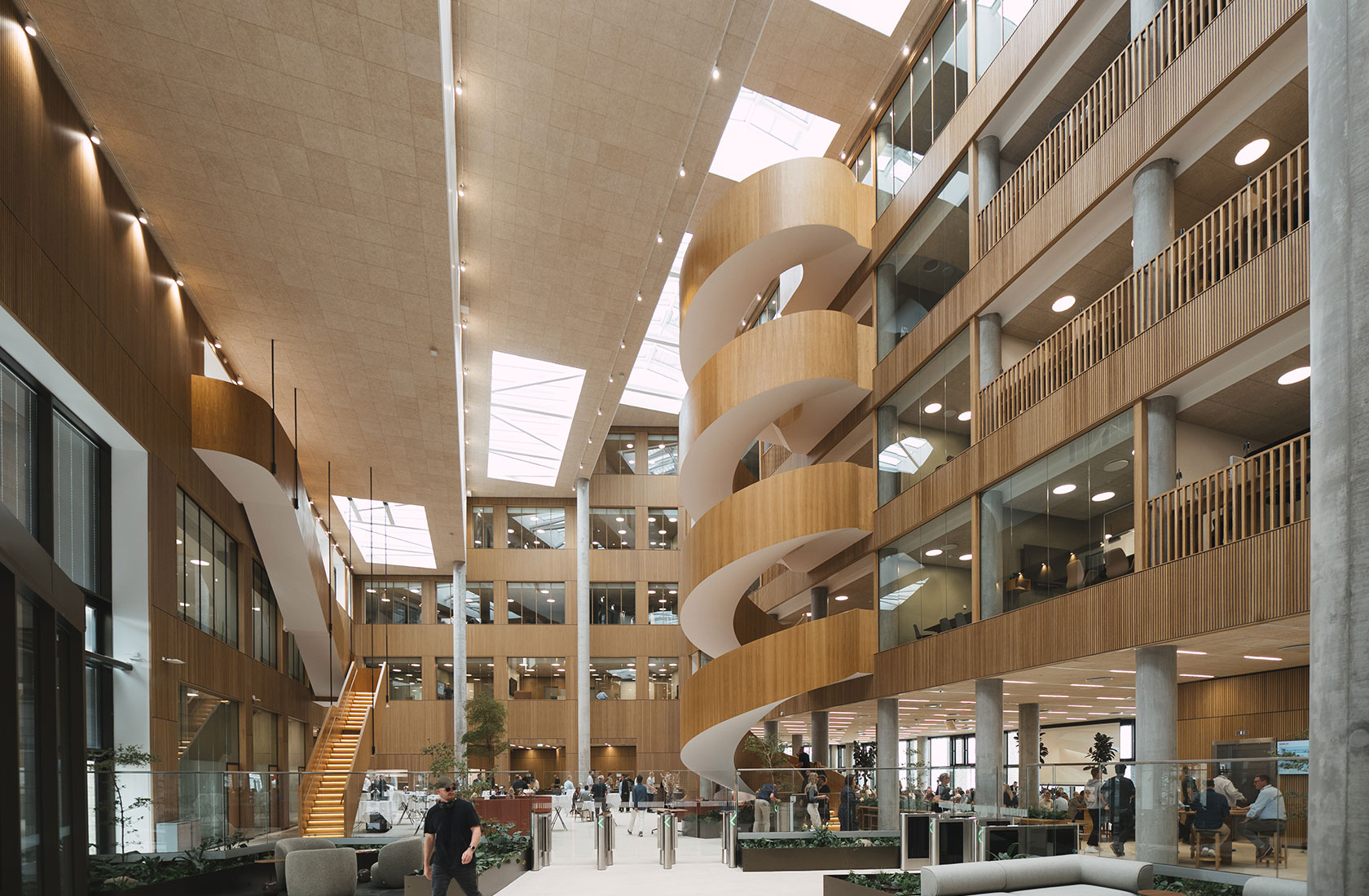 Modern multi-story office building interior with spiral staircase and glass walls, people walking.