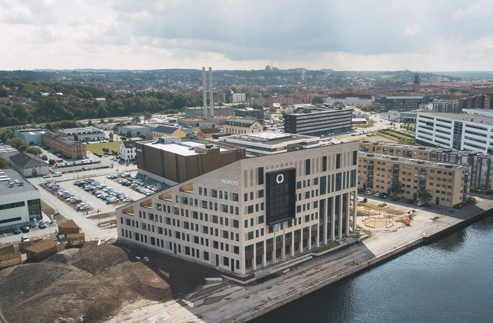 Aerial view of Norlys headquarters, modern building near water in industrial cityscape.