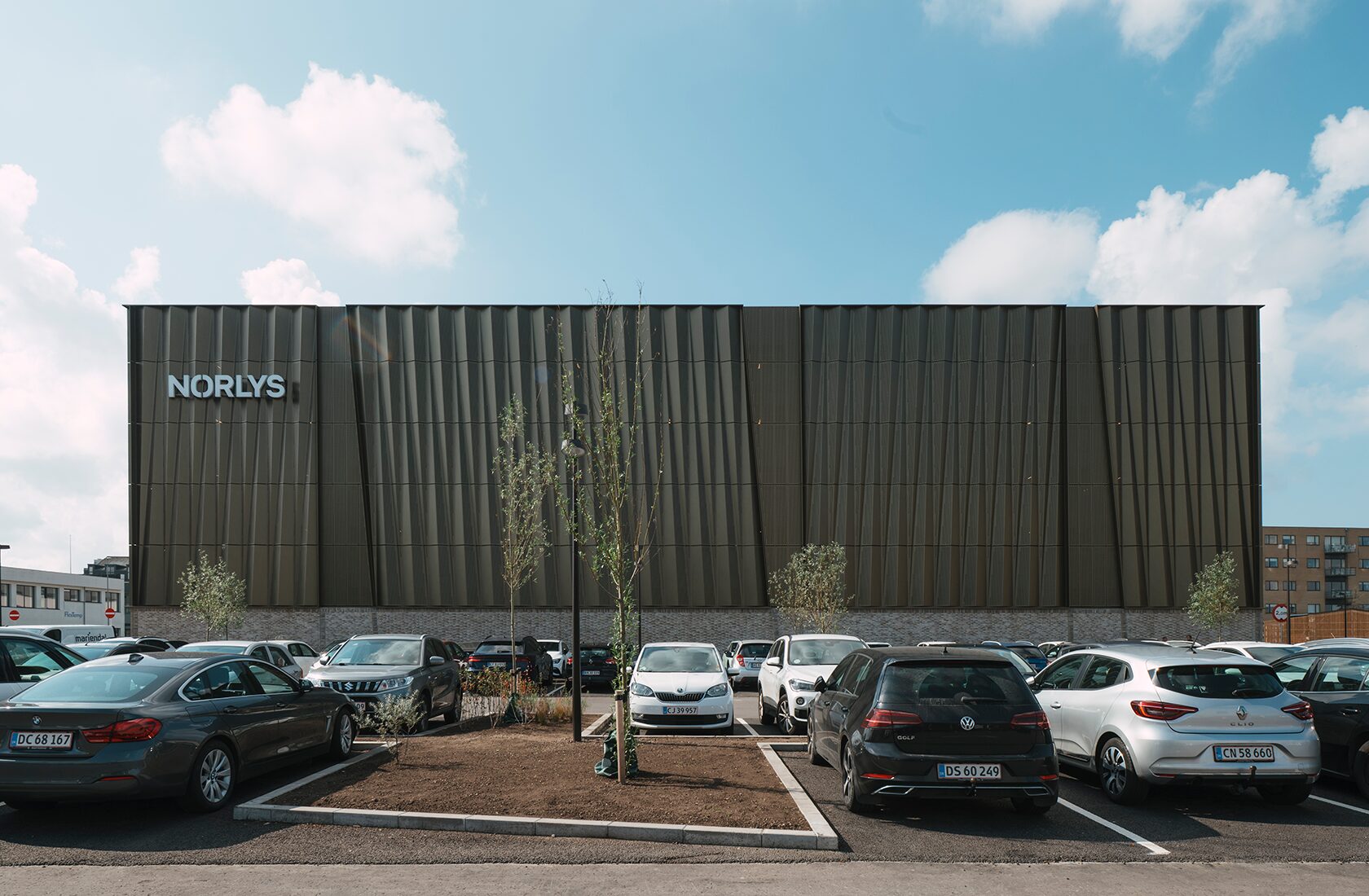 Modern Norlys building with parked cars and trees in the foreground against a blue sky background.