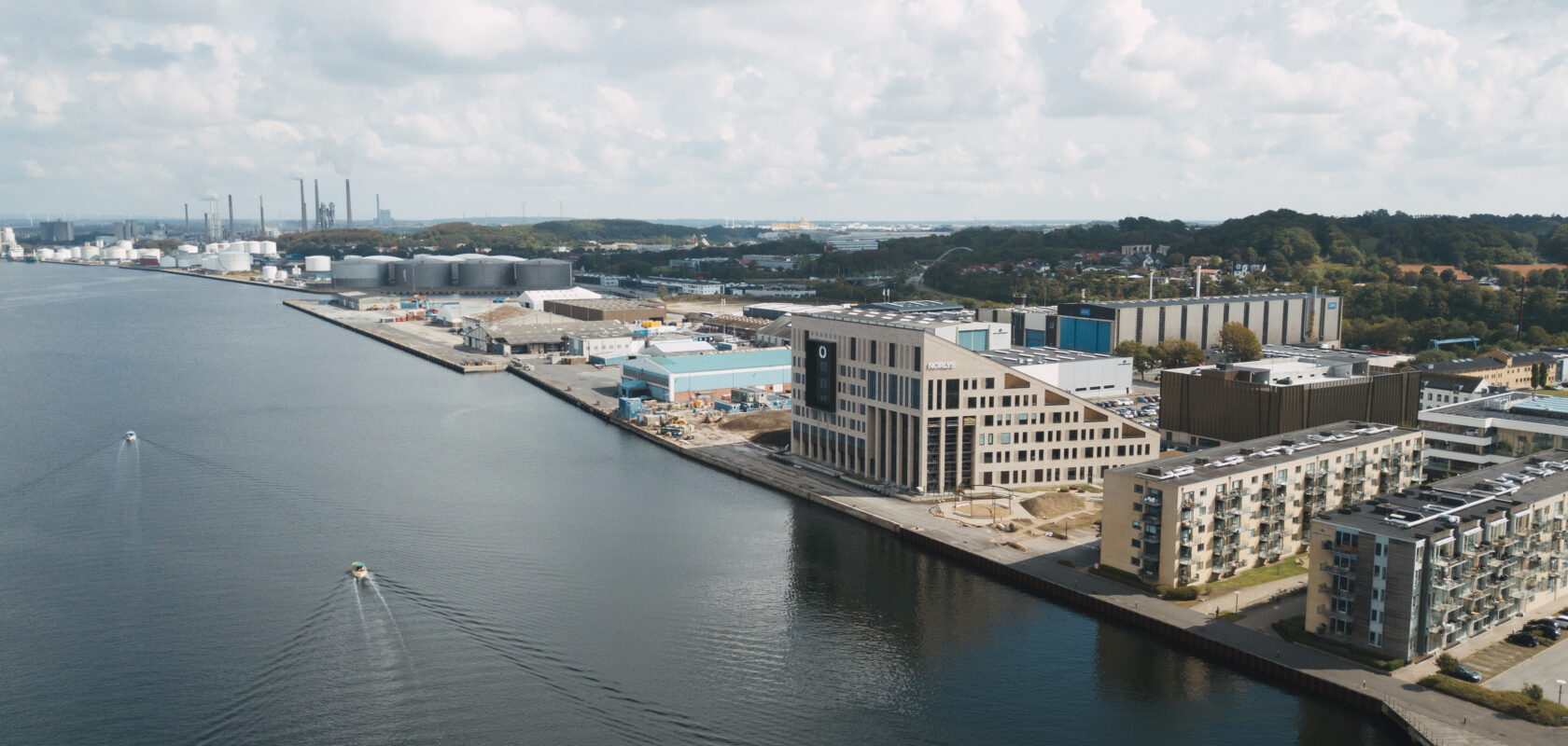 Aerial view of harbor with modern buildings, industrial tanks, and boats on a sunny day.