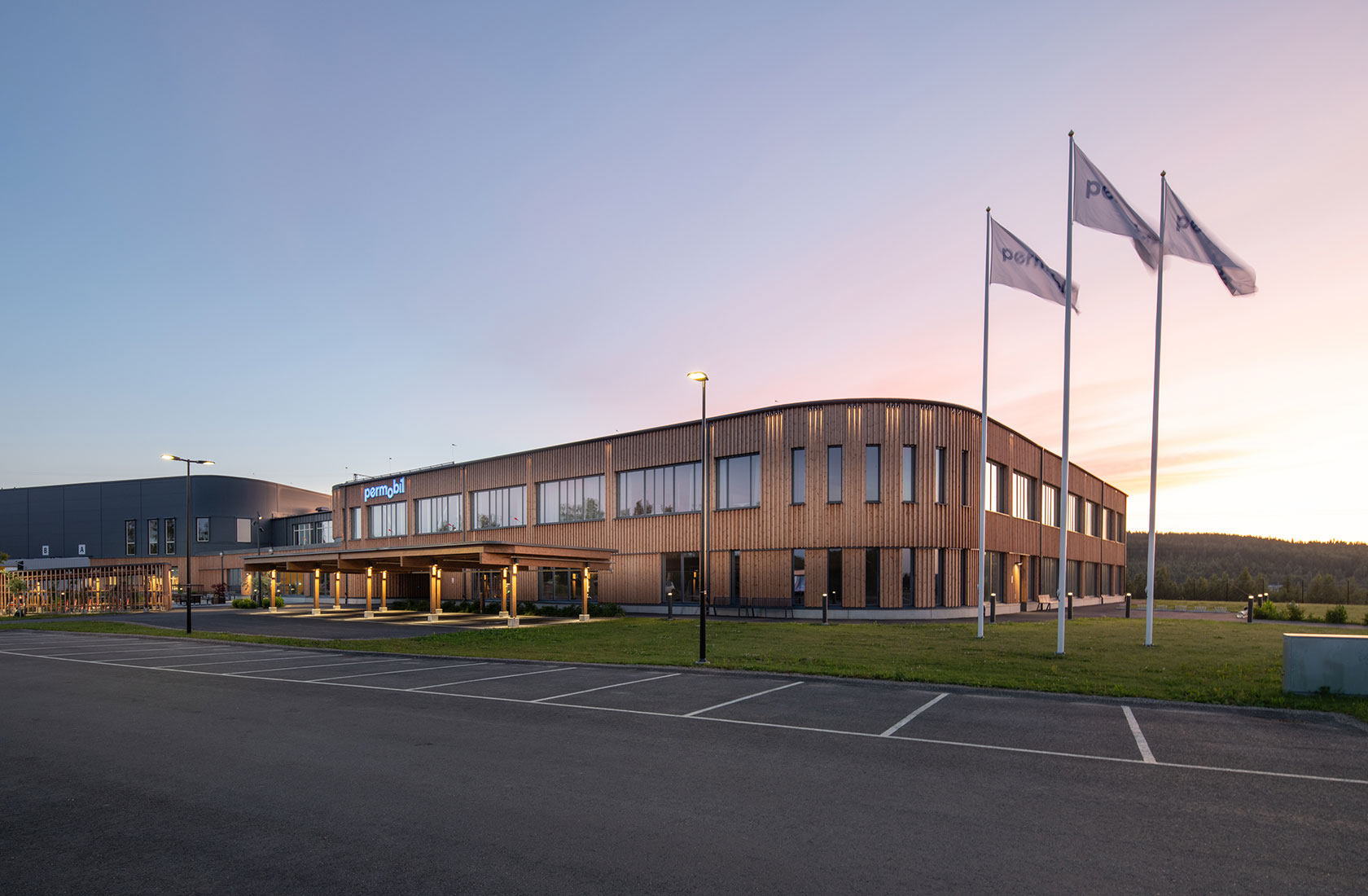 Modern office building with wooden exterior, flags, and parking lot at sunset.