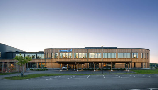 Modern office building with "permobil" signage, large windows, and wooden exterior at sunset.