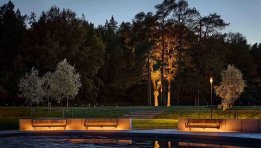 Cementery park at twilight with illuminated benches, reflecting pool, and trees in the background.