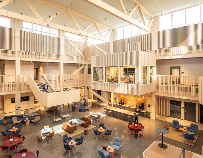 Modern office lobby with wooden architecture, open seating area, and large windows.