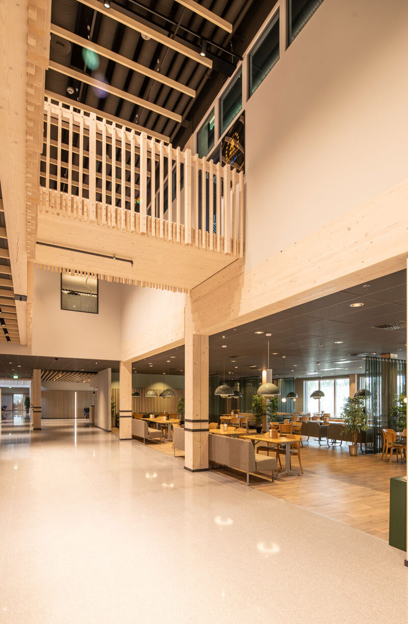 Modern interior space with wooden accents, high ceilings, and a seating area with tables and plants.