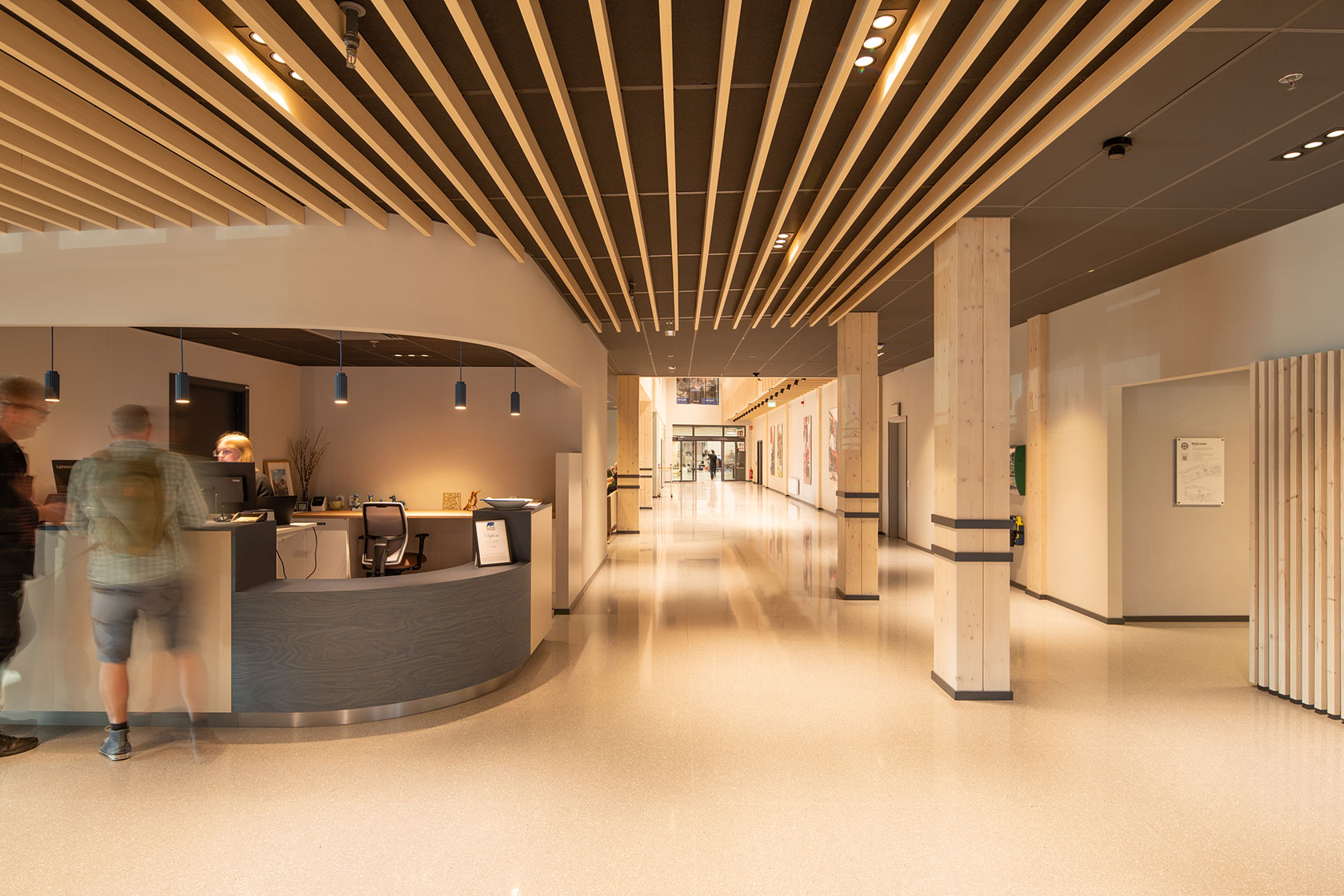 Modern reception area with wooden ceiling, elegant lighting, and polished floors.