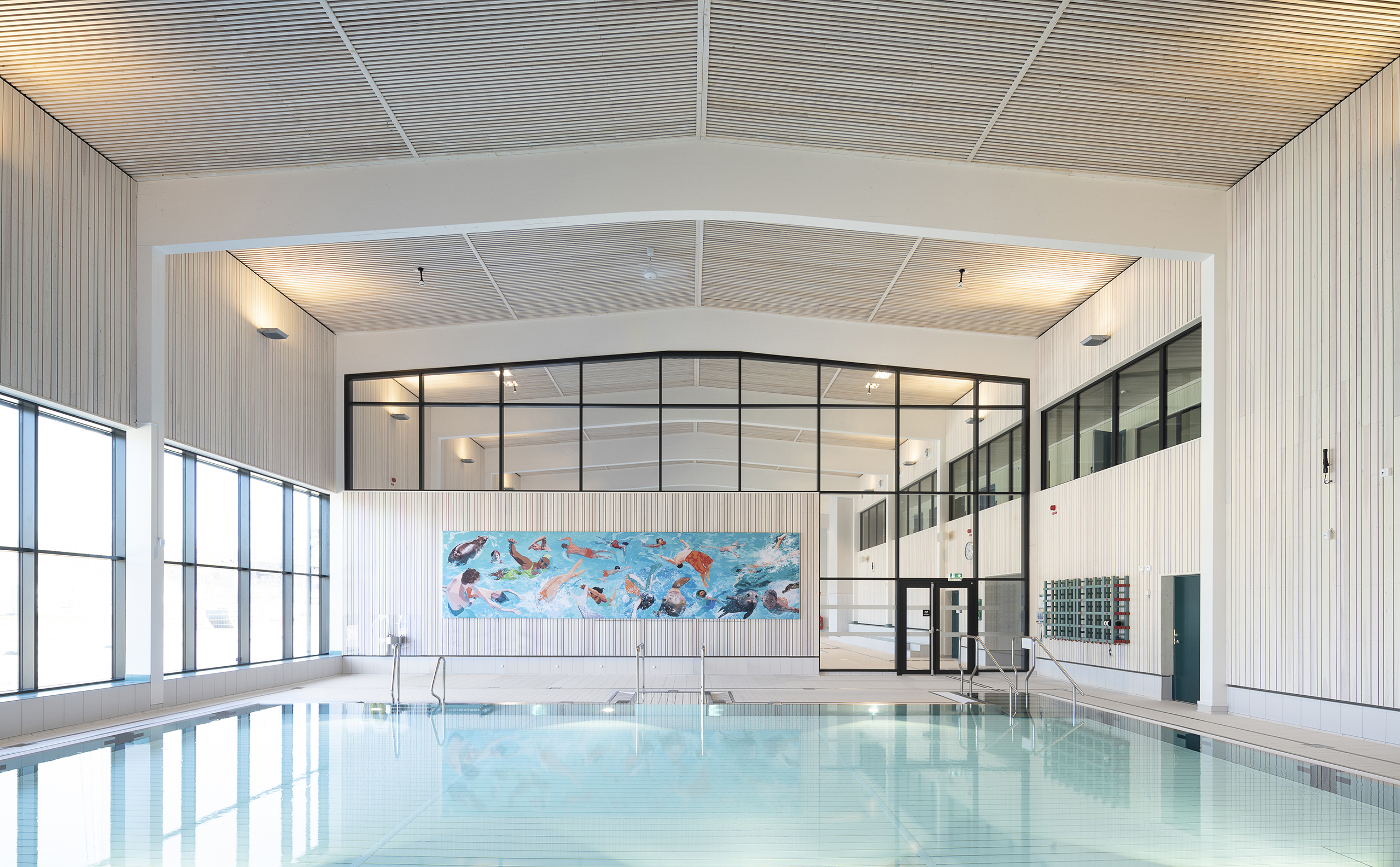 Indoor swimming pool with large windows and a vibrant mural on the back wall in a modern facility.