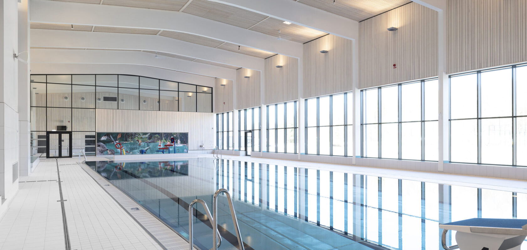 Indoor swimming pool with large windows and a diving board. Modern, bright and spacious design.