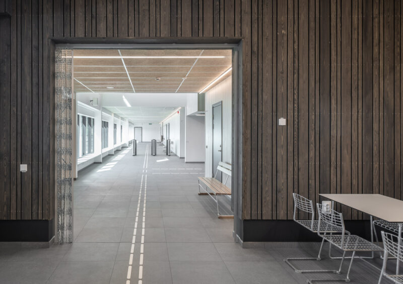 Modern hallway in a swimming facility with wood-paneled walls, large windows, and sleek furniture in a minimalist building.