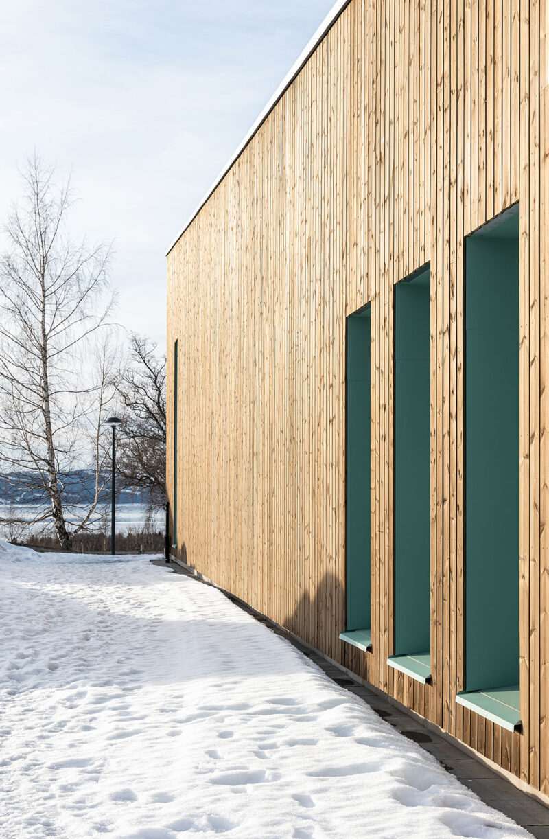 Modern wooden building with snow-covered path and bare trees in winter.
