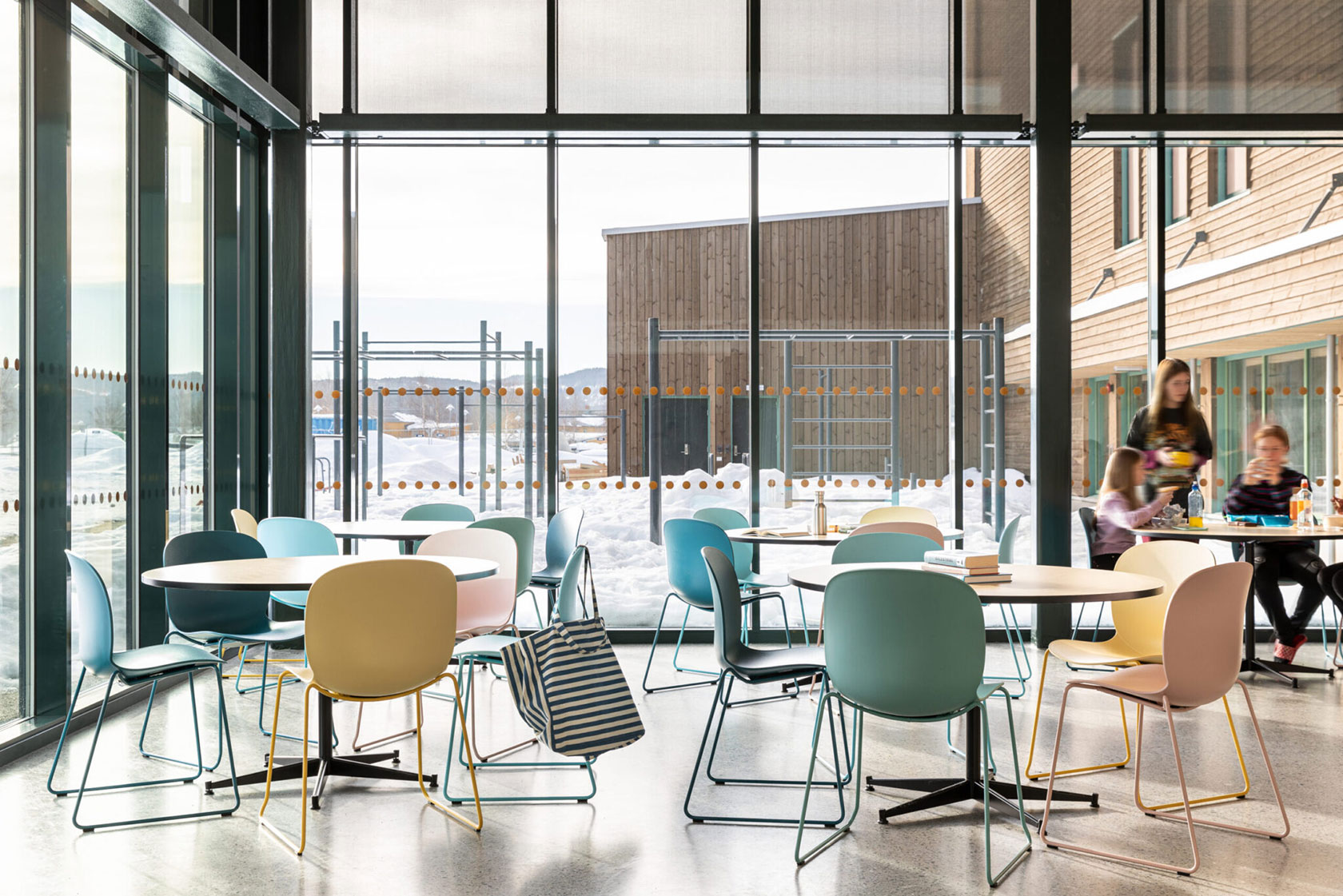 Modern school cafeteria with colorful chairs, large windows, and a snowy outdoor view.